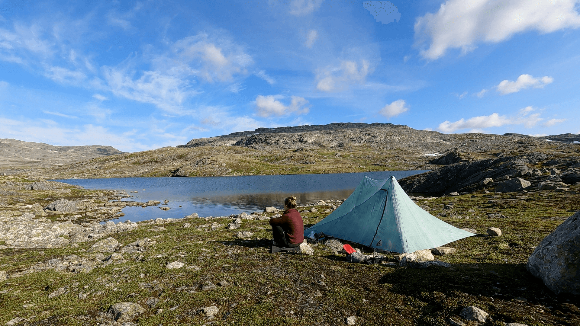 Frau sitzt mit Dynemma Zelt in karger Landschaft an einem kleinen See