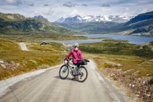 Highlights mit pinker Regenjacke auf Gravelstrasse mit See und Bergen im Hintergrund